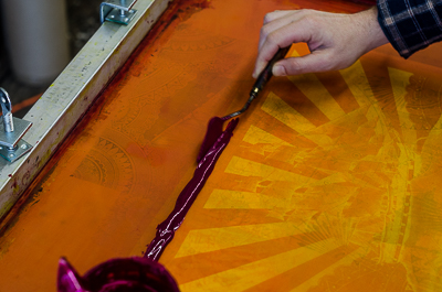 After rinsing off the ink from the screen and waiting for it to dry, Beau Stanton applies the magenta ink on one side of it